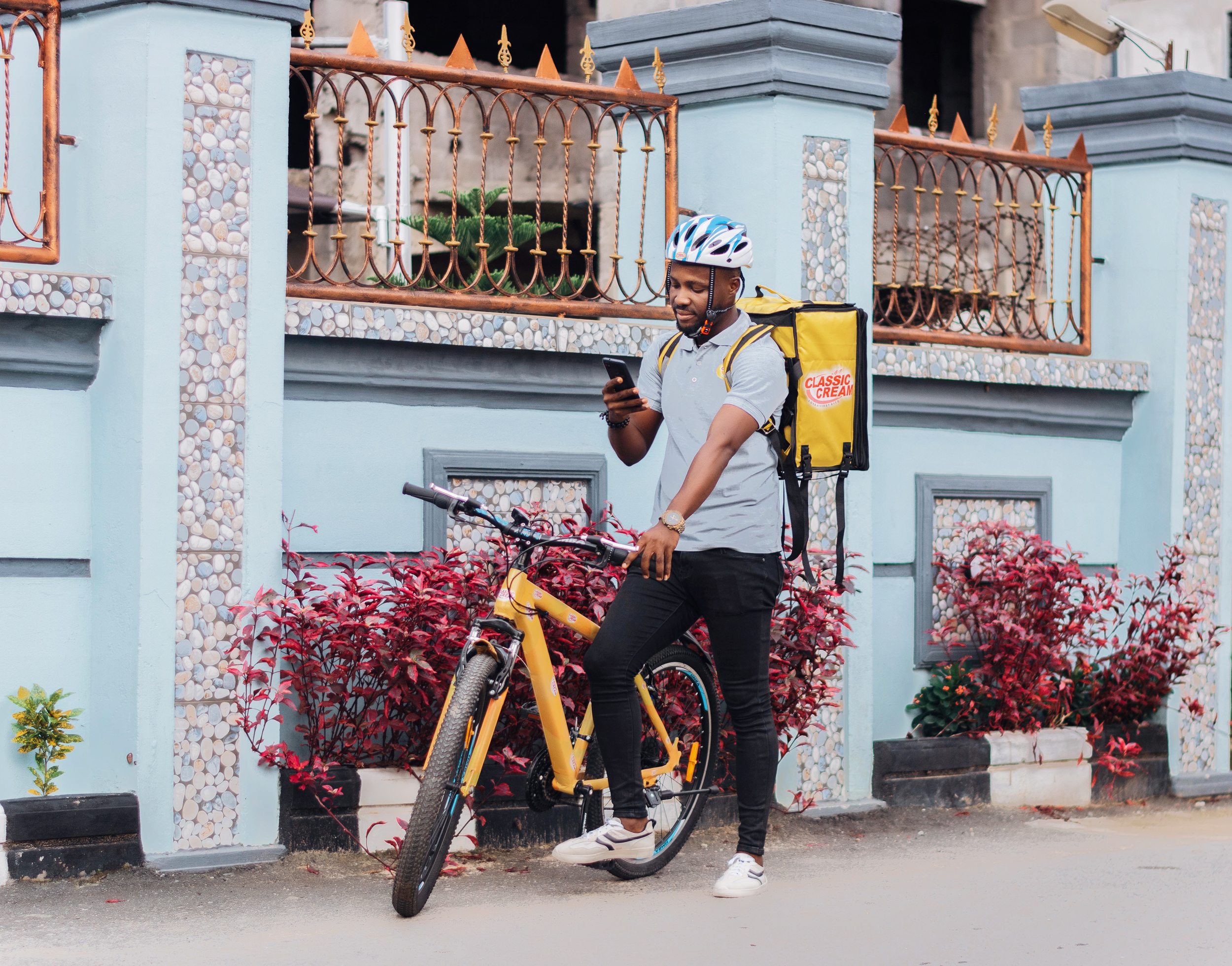Bicycle courier checks phone beside yellow bike and insulated delivery bag.
