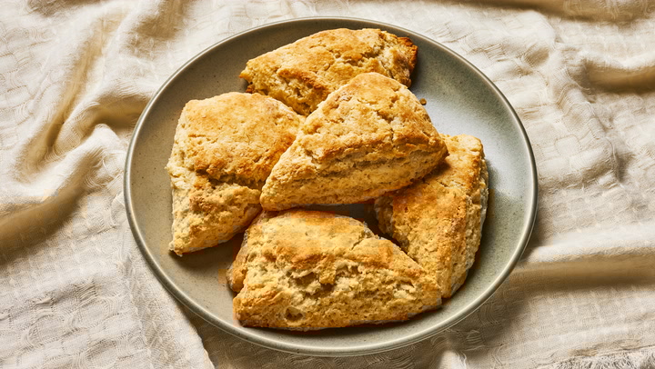 Golden triangular scones arranged on gray ceramic plate over linen cloth.